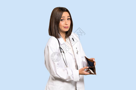 年轻女医生手拿着钱包的蓝背景孤图片
