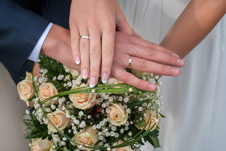 新娘和新郎的手放在婚礼花束上图片