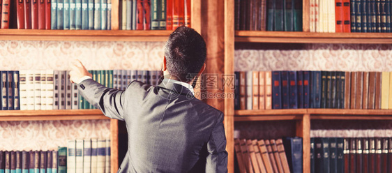 男人从书柜里拿书学生站在图书馆里选择书穿着漂亮西装的家伙在书柜附近看书学习学习教育研究历史文学智慧概图片