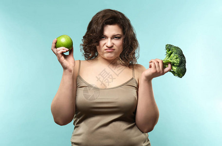 带着苹果和花椰菜色背景的超重女不高兴背景图片
