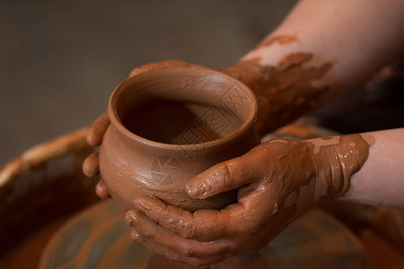 从上面拍摄的旋转陶轮和陶器A用泥杯雕刻双手中的粘土的图片