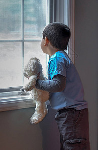 一个带着毛绒熊的小男孩看着窗图片