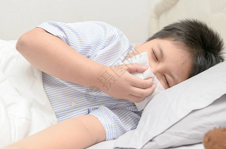 生病的男孩用组织抽鼻子躺在床上生病和图片