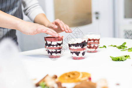 一个糖果商在三个杯子里准备一个小东西甜点在厨房的白色桌子上自制糕点烹图片