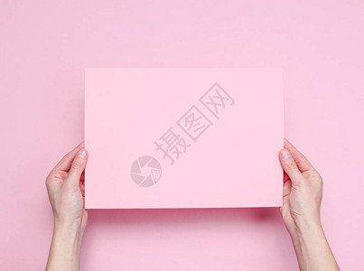 女手握着粉红背景的粉红色纸页图片