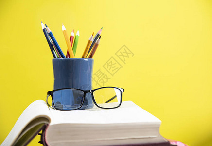 图书馆黄色背景教育概念书中的铅笔盒和眼镜上的彩色铅笔图片