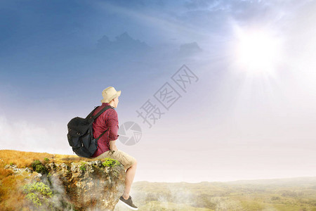 仰望有阳光背景的风景观视着亚洲旅行者在悬崖边缘上坐着帽子图片