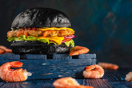 虾堡芝士汉堡配虾在木制蓝色背景上的黑色小圆面包背景