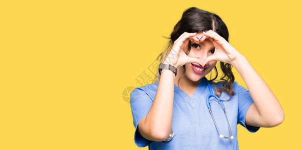 身穿医疗制服的年轻成年女医生以手和指笑着微笑的表情展现心图片
