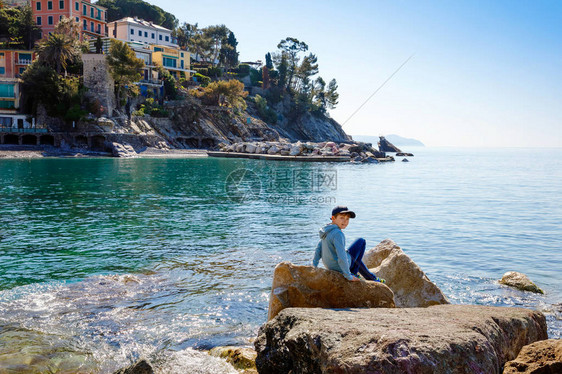 小男孩在意大利古里亚地区的地中海滩上攀爬石头图片