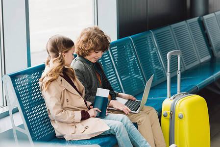 儿童坐在机场候诊大厅黄色手提箱附近的蓝色座位上图片