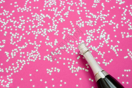 香槟瓶与全息五彩纸屑星在明亮的粉红色背景图片