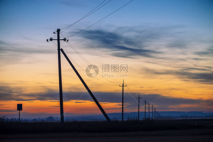日出背景场中的电源线黎明时分电线杆的剪影温暖的橙色蓝天上的高压电缆夕阳下的电力行业五彩如图片