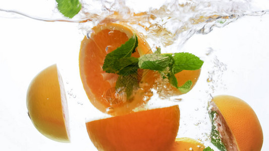 鲜切多汁橙子和大量薄荷叶落下在清水中喷洒白色背图片