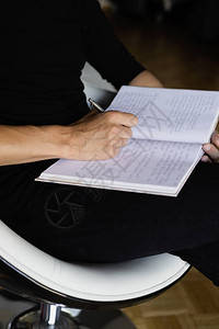 一名身着黑色散衣穿着笔记本在室内椅子上用笔写字的年轻天主教图片