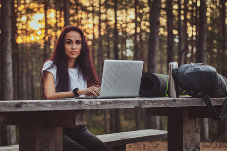 美丽的年轻女子正在森林中央的笔记本电脑上工作图片