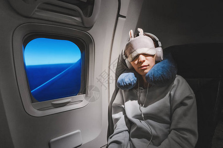 亚洲女孩睡在飞机上靠近窗户的座位上图片