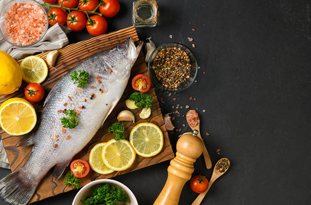 新鲜的鱼鲈和烹饪配料黑石板桌上有香料和香草的生鱼鲈海鲜图片