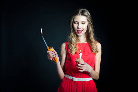 穿着红裙子的年轻美女肖像拿着生日纸杯蛋糕一根蜡烛和汽油打火机图片