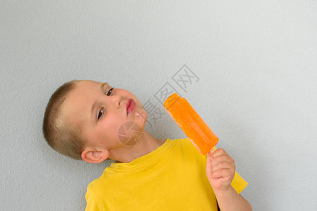 一个穿黄色T恤的小男孩拿着橙色冰淇淋在一根棍子上叫爱斯基摩人一图片