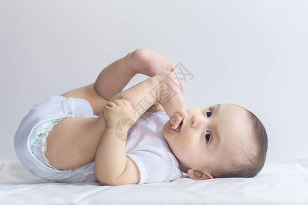 饥饿的小男孩把脚放在嘴里6个月大的婴儿在白色床上用品玩得开心可爱的宝躺在床上图片