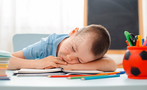 男生坐在家里的教室躺着桌子上摆满了书籍培训材料学童睡觉懒惰无聊缺乏能量疲劳概念沉迷和鬼图片