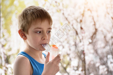 男孩在开花树背景上呼吸面具吸入器时吸气图片