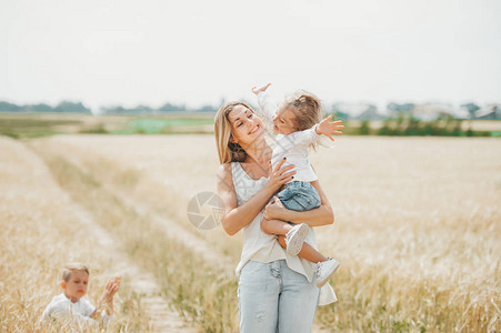 母亲在麦田抱着一个微笑的小女孩儿子坐在之间母背景图片