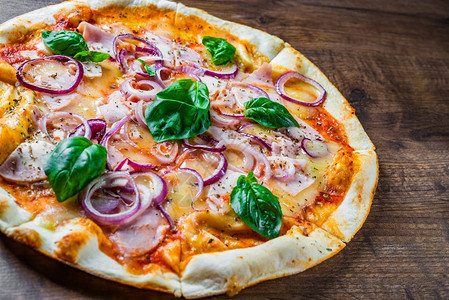 披萨配马苏里拉奶酪火腿番茄酱洋葱胡椒香料和新鲜罗勒在木桌背景图片