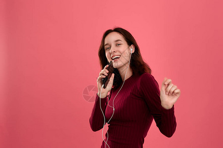 快乐的年轻黑发女人唱歌和跳舞用智能手机作为麦克风图片