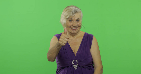 一位老妇人竖起大拇指微笑一件紫色礼服的老俏丽的祖母放置您的徽标或文本色度图片