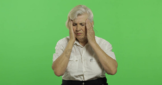 一位年长的妇女因头痛而苦一件白衬衫的老俏丽的祖母放置您的徽标或文本色度键绿屏背景图片