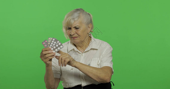 一位老妇人不满地看着水泡丸一件白衬衫的老俏丽的祖母放置您的徽标或文本色度键绿屏背景图片