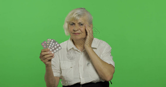 一位老妇人不满地看着水泡丸一件白衬衫的老俏丽的祖母放置您的徽标或文本色度键绿屏背景图片