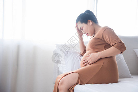 中年孕妇坐在床上因高血压高血压而头痛图片