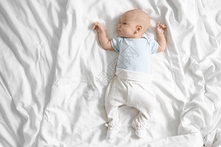一个3月大的婴儿身穿蓝体装的顶端风景躺在一张白色软床图片