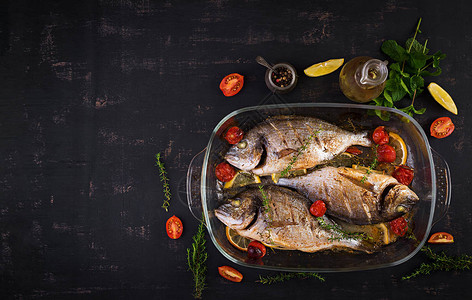 烤鱼多拉与柠檬和香草在烤盘上深色乡村背景顶视图与鱼概念的健康晚餐节图片