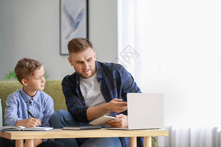 父亲帮助儿子在家上课图片