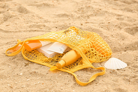 带防晒霜的袋子和沙滩上的书图片