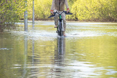 赤脚骑自行车的人试图在春天的洪水中克服随着河水冲破河岸图片