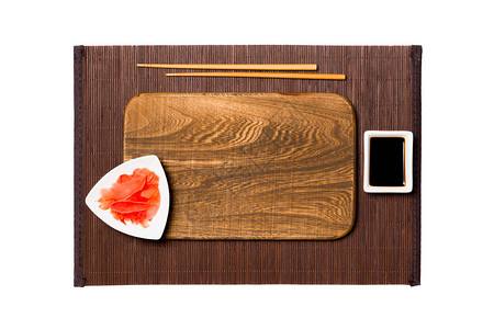 深色竹垫背景上带筷子的空长方形棕色木盘图片