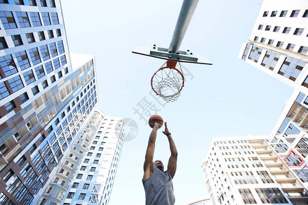 城市背景下非洲篮球运动员在天空中扣篮的低角度动作镜背景图片