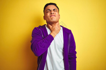 身穿紫色运动衫的巴西年轻男子站在孤立的黄色背景上摸着脖子痛喉咙痛图片
