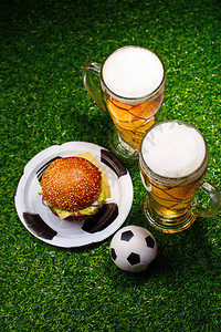 两杯啤酒汉堡包和足球放在绿草地图片