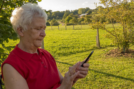 高龄公民在花园的手机上检查您的留言请访问InfoF图片