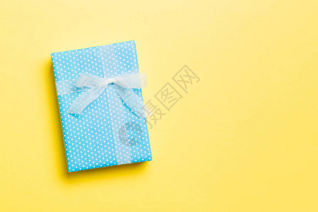 用黄色背景上的白丝带用纸包裹圣诞节或其他节日手工制作的礼物图片
