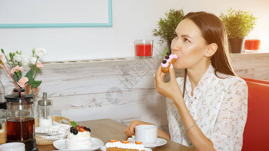 穿暑期服装的快乐女孩吃着美味的蛋糕在现代甜点店桌边盛图片