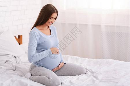 怀孕在卧室睡觉的孕妇快乐期待的女士触摸着Belly和S图片