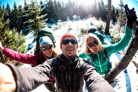 三名游客的自拍照朋友一起旅行徒步穿越冬天的山脉两个女人和一个背着包的男人正穿过白雪覆盖的森林背景图片