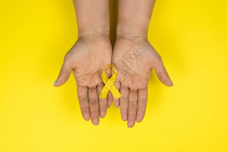 黄色背景的女孩手中的黄金丝带儿童癌症概念宣传月儿童癌症日2图片